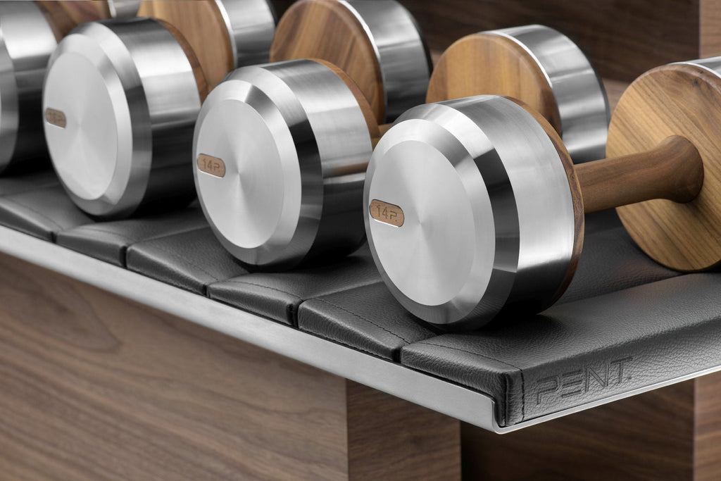 Dumbbells with bright silver ends resting on a black padded rack against a wood-paneled wall