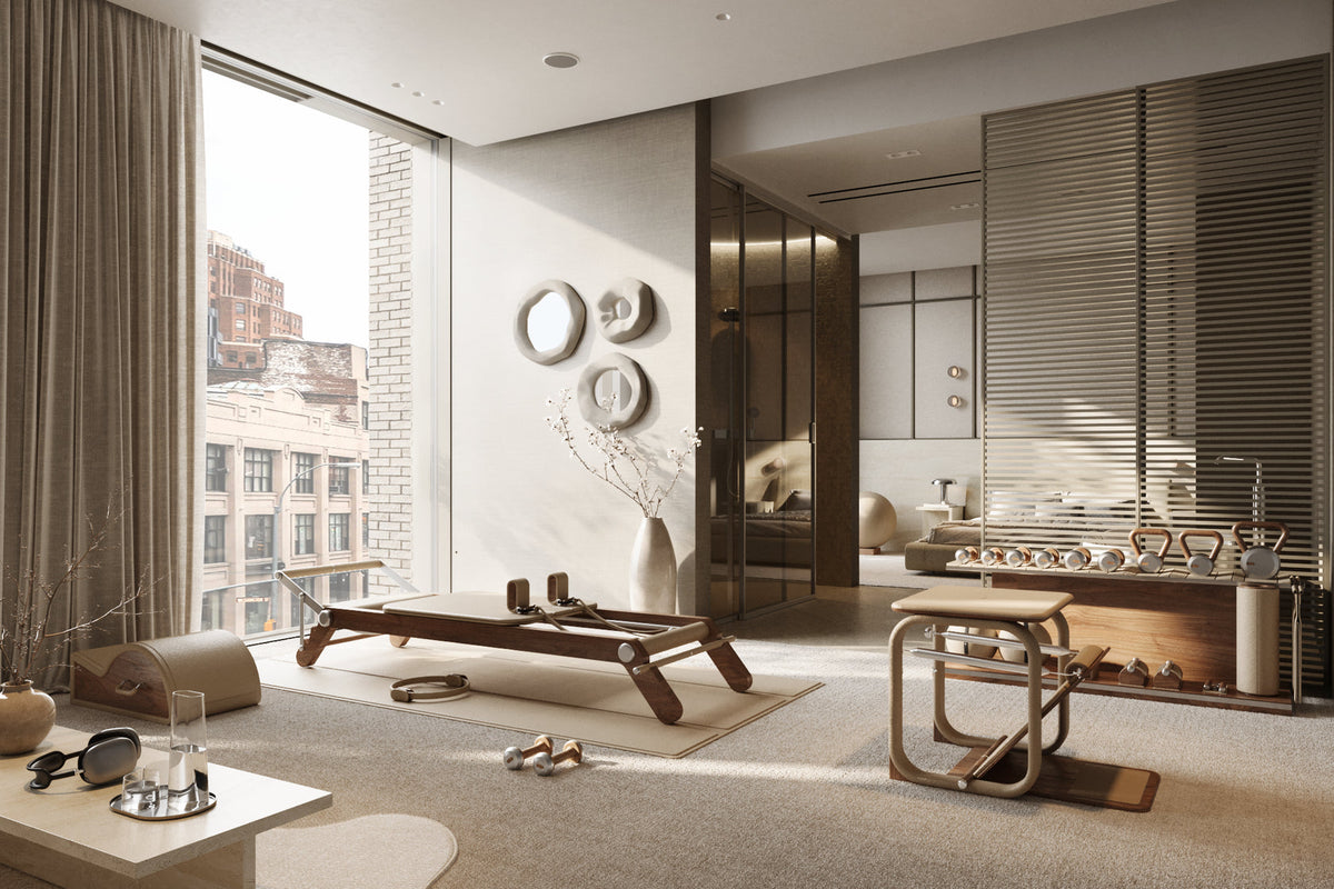 Bright exercise room with a Pilates reformer, chair, dumbbells and balance barrel by windows
