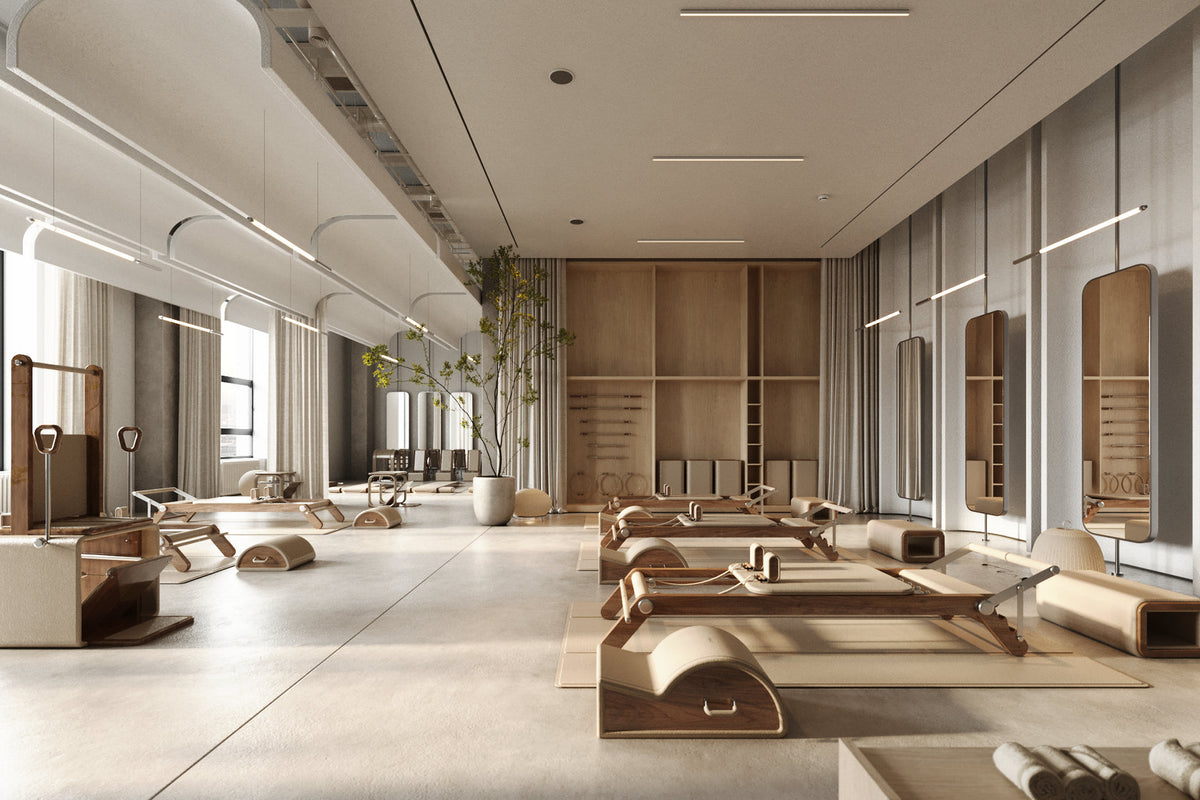 Pilates studio with several reformer machines, mirrors, mats and a potted tree under pendant lights