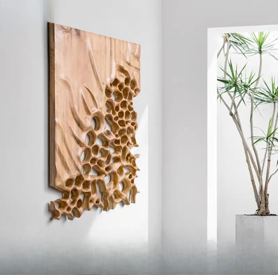 Carved tan wall panel with honeycomb-like openings mounted on a gray wall beside a window