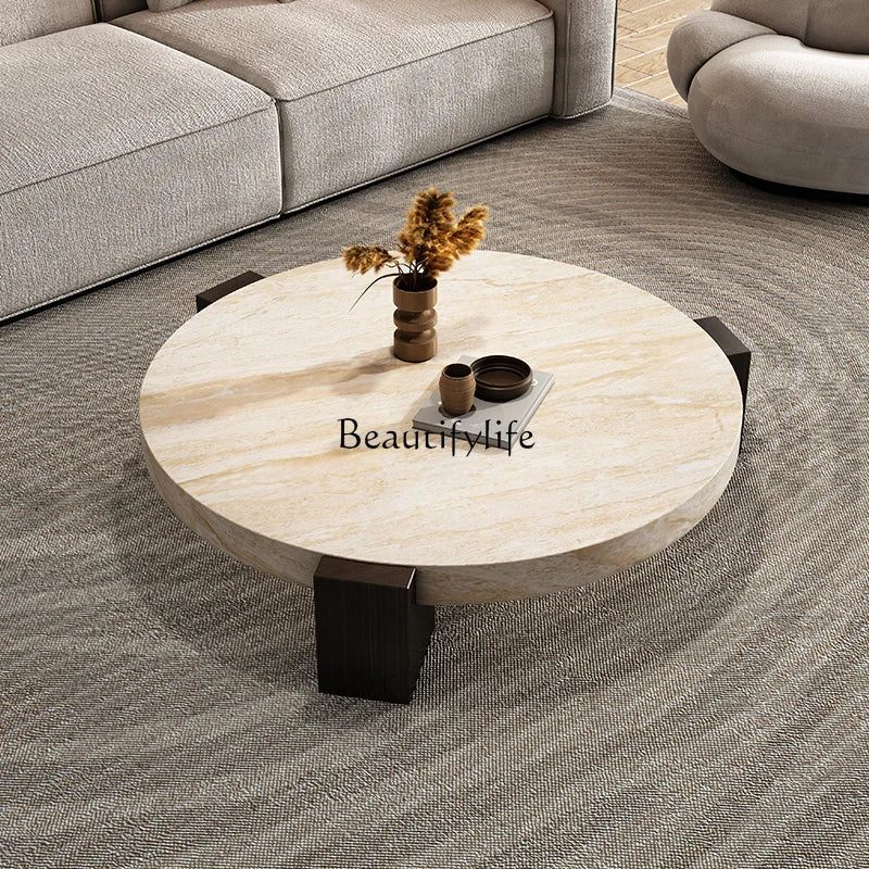 Round travertine-finish coffee table styled in a living room with a sofa and dried flower arrangement