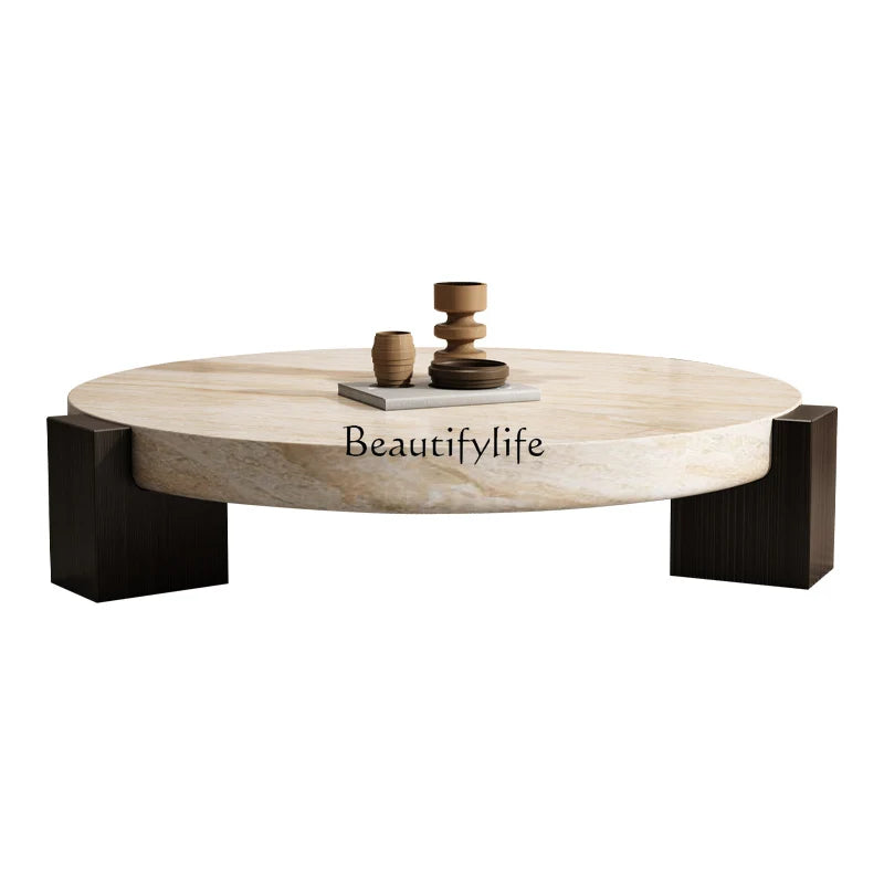 Round travertine-finish coffee table with dark wood legs and decorative accent pieces on a white background
