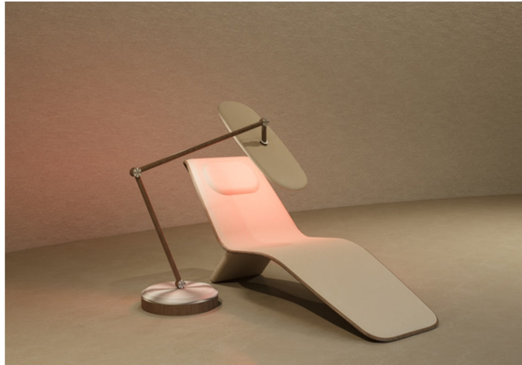 Beige reclining chaise lounge with head cushion beside a dark floor lamp, warm light glowing