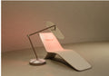 Beige reclining chaise lounge with head cushion beside a dark floor lamp, warm light glowing